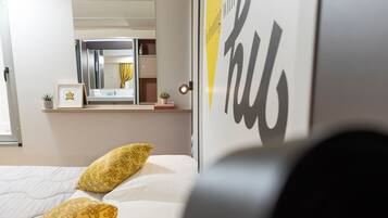Habitación de hotel con cama, mesita de noche con lámpara, espejo y ventana.