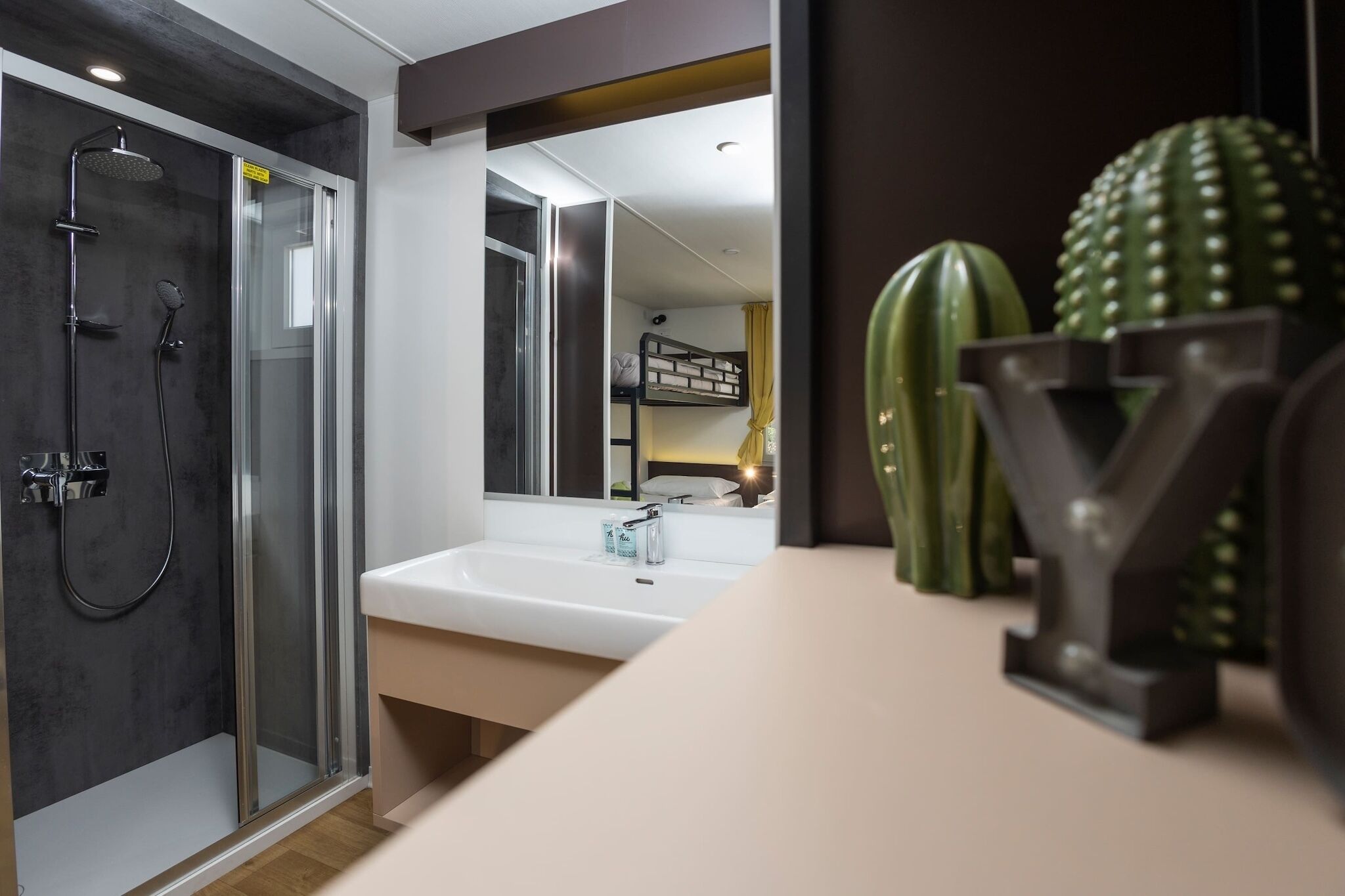 Un baño moderno con ducha acristalada, lavamanos blanco y un espejo grande.