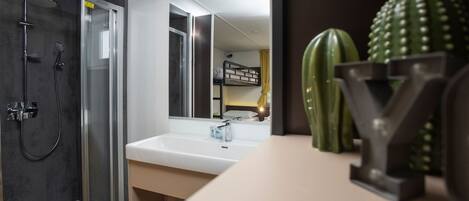 Un baño moderno con ducha acristalada, lavamanos blanco y un espejo grande.
