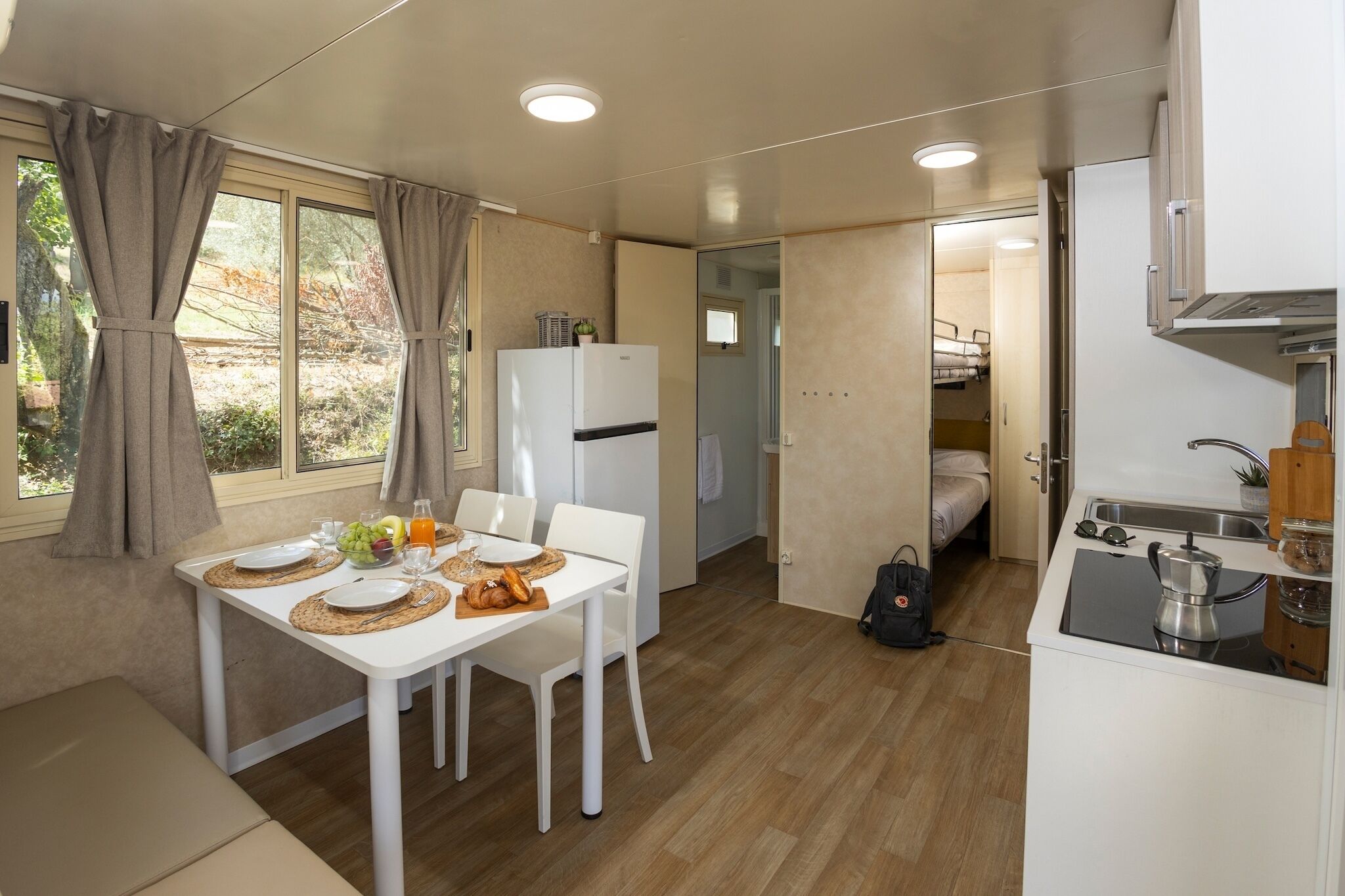 A compact kitchen with a dining area, a refrigerator, a sink, and a small sleeping area.
