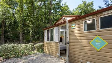 A small, single-story wooden cabin with a door open, revealing a bed inside.