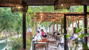 Un espace de restauration en plein air avec des tables et des chaises en bois, des guirlandes lumineuses et une vue sur la verdure.