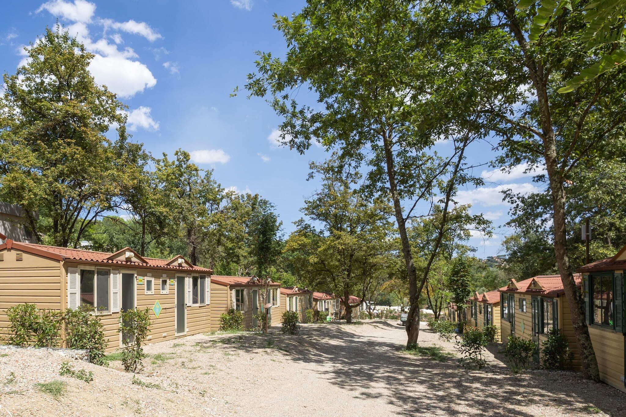 Une rangée de cabanes en bois aux toits rouges, entourées d’arbres et sous un ciel dégagé.