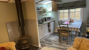 Una cocina acogedora con estufa de leña, una mesa de comedor con sillas y una ventana con vistas al exterior.