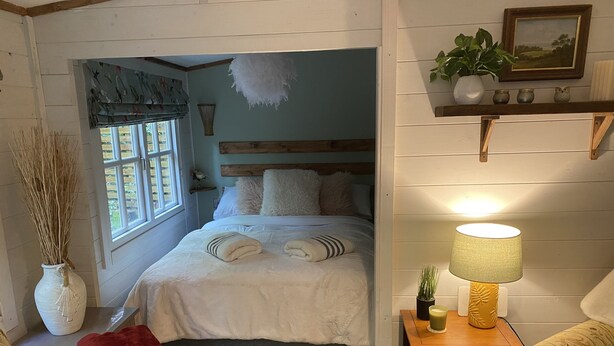Un dormitorio acogedor con cama, mesita de noche, lámpara y ventana con cortinas.