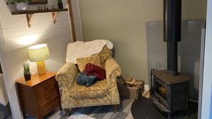 Una habitación acogedora con una silla de madera, una lámpara, una chimenea y un estante con plantas y un cuadro.