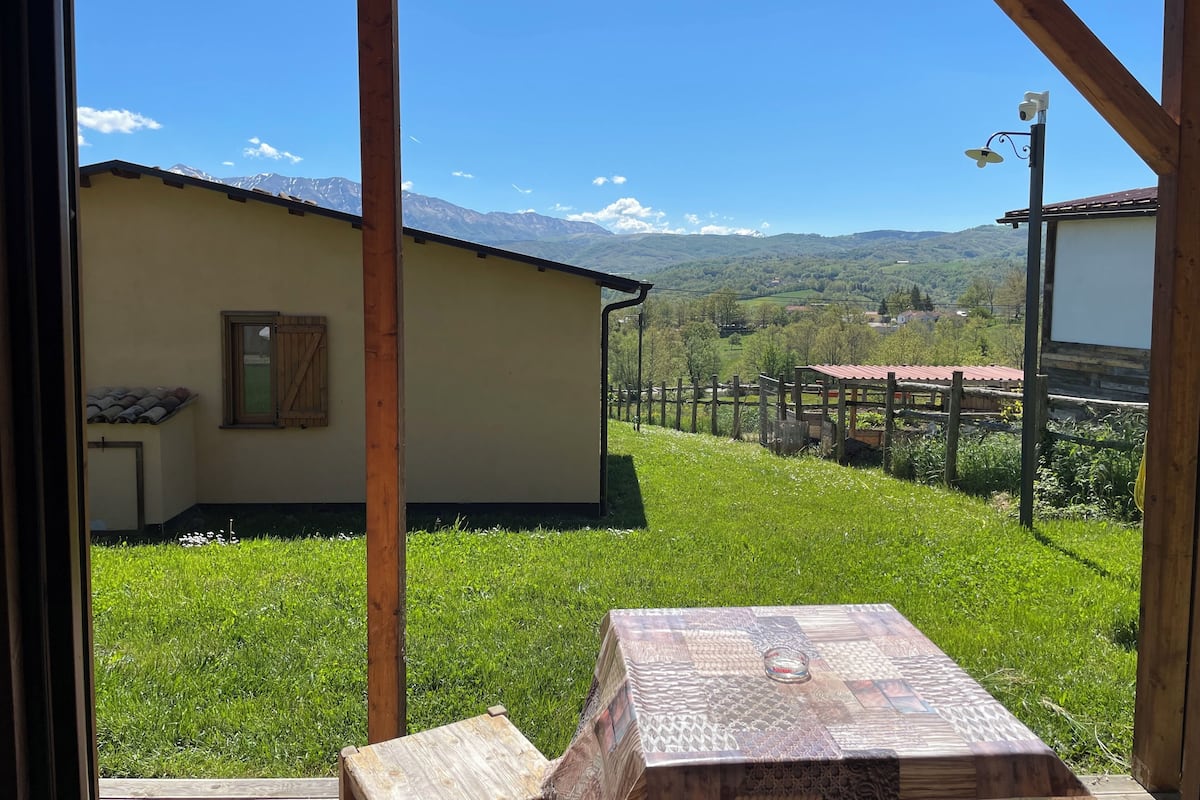 A wooden structure with a table and chairs, a wooden fence, and a view of a mountain range.