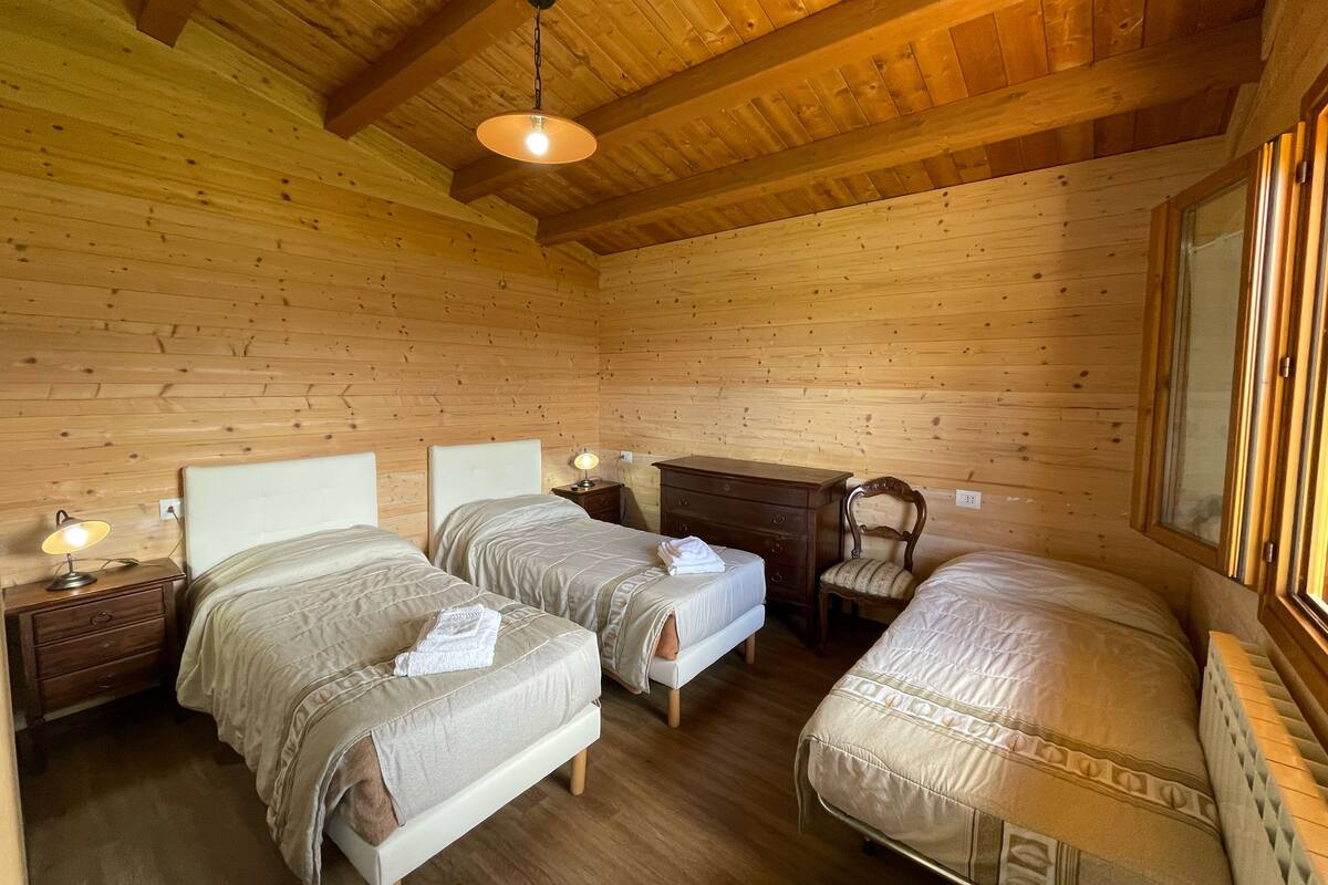 A wooden cabin bedroom with two beds, a nightstand, a dresser, and a chair.
