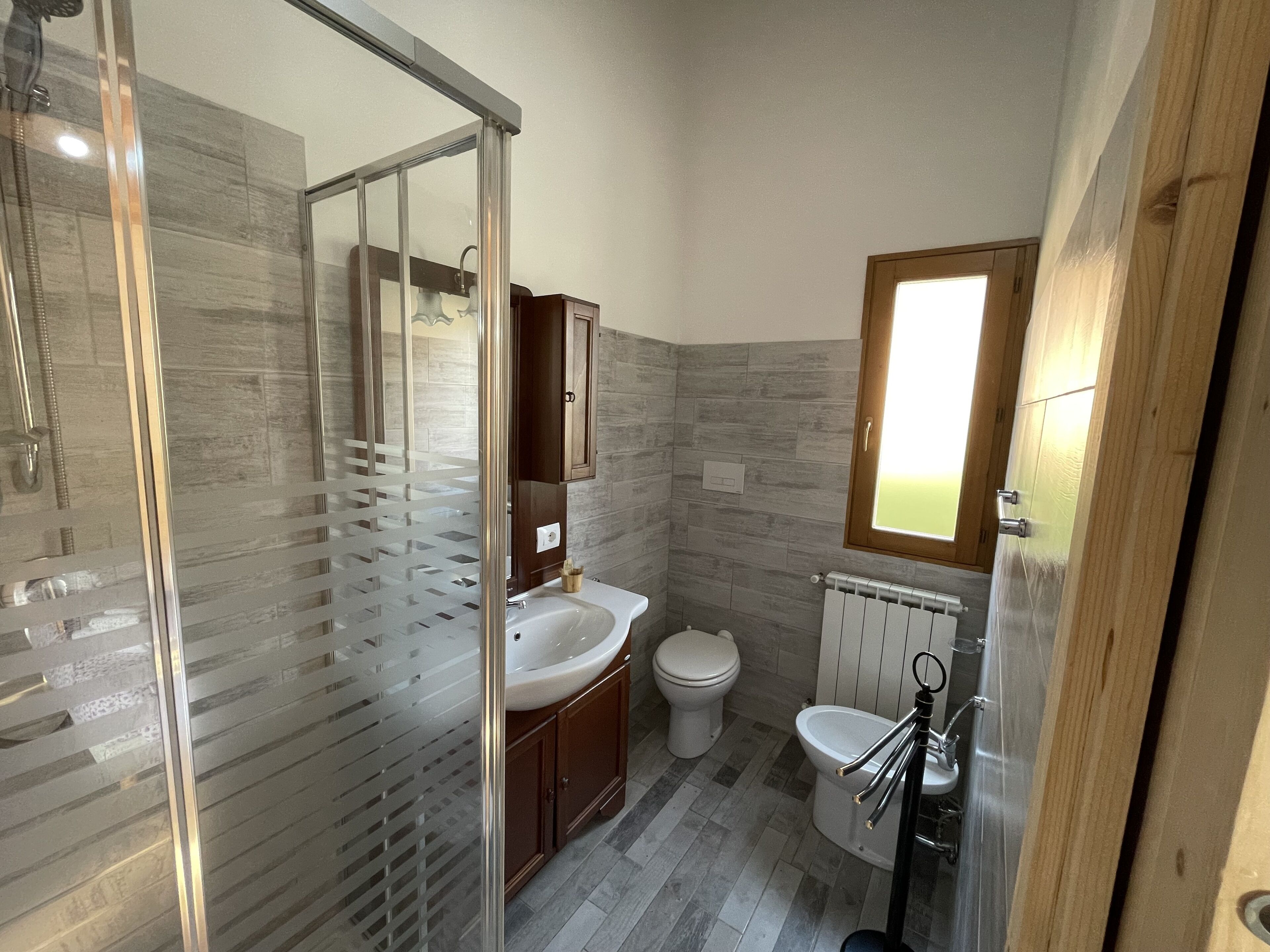 Un baño moderno con cabina de ducha de vidrio, lavamanos, inodoro y bidé.