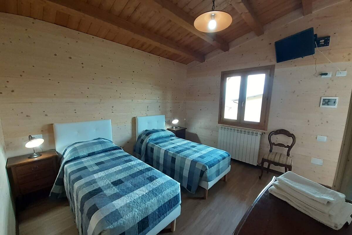 A cozy room with two beds, wooden walls, a window, a radiator, and a chair.