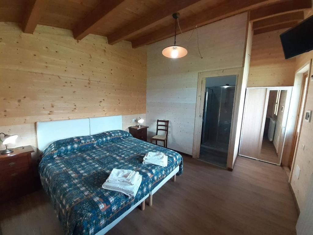Une chambre avec un plafond en bois, un lit recouvert d’une courtepointe à motifs bleus, une table de chevet avec une lampe et une chaise.