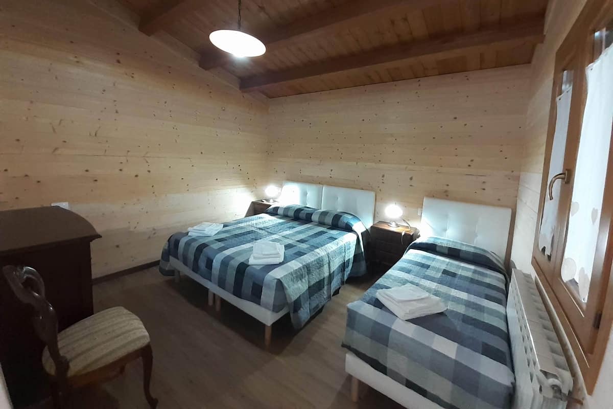 A wooden cabin room with two beds, a desk, and a chair.