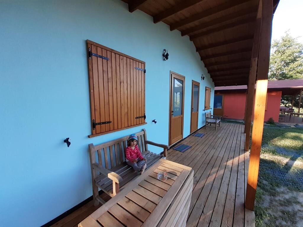 A covered wooden deck with a bench and a child sitting on it.