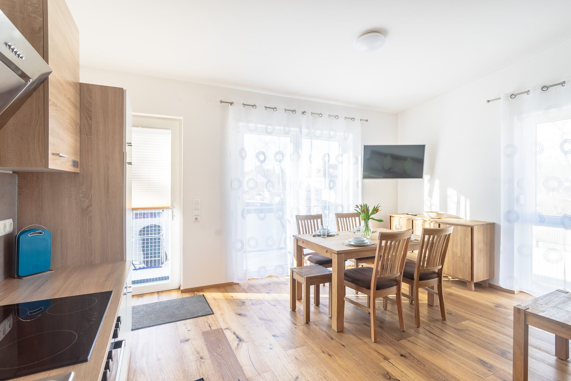 A modern kitchen with wooden cabinets, a built-in stove, and a blue suitcase on the counter.