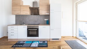 Une cuisine moderne avec des meubles en bois, une hotte en acier inoxydable, un four encastré et une fenêtre pour laisser entrer la lumière naturelle.