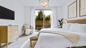 A bedroom with a bed, a dresser, a TV, and a balcony with a view of trees and a fence. - Sunset Oasis: GameRoom, Heated Pool, Hot Tub Gate Community (Indio)