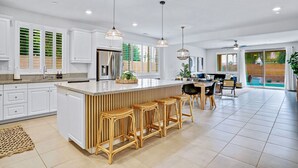 A spacious kitchen with white cabinets, a large island with bar stools, and pendant lighting. - Sunset Oasis: GameRoom, Heated Pool, Hot Tub Gate Community (Indio)