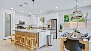 A modern kitchen with white cabinets, stainless steel appliances, and a central island with bar stools. - Sunset Oasis: GameRoom, Heated Pool, Hot Tub Gate Community (Indio)