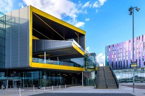 Ein modernes Gebäude mit einer gelb-schwarzen Fassade, großen Glasfenstern und einer Treppe, die zu einer oberen Ebene führt.