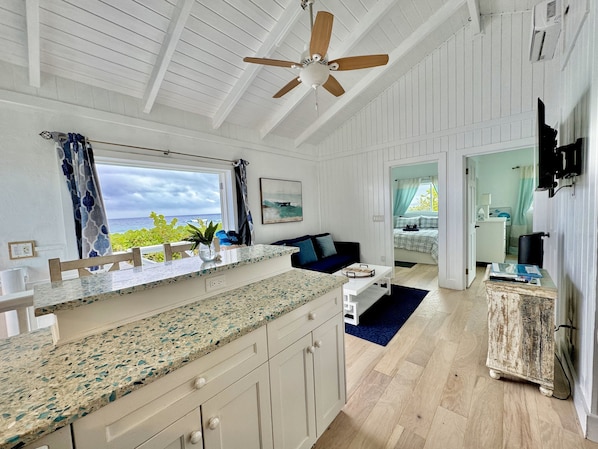 Una cocina amplia con una isla grande, un ventilador de techo y vista al océano a través de una ventana.