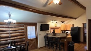 A cozy kitchen with wooden walls, a dining area with chairs, a bar with stools, and a refrigerator. - Charming "Vintage" Style Mountain Cabin Under the Pines (Almont)