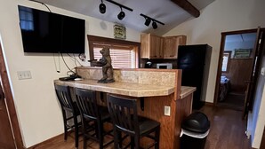 A kitchen with wooden cabinets, a black refrigerator, a countertop with a bear sculpture, and a TV mounted on the wall. - Charming "Vintage" Style Mountain Cabin Under the Pines (Almont)