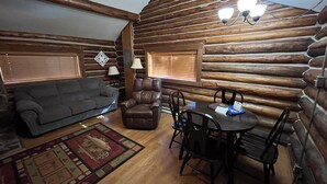 A log cabin interior with a sofa, armchair, dining table, and chairs. - Charming "Vintage" Style Mountain Cabin Under the Pines (Almont)