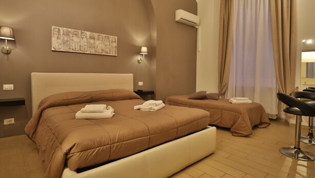 Habitació d'hotel amb un llit gran, un llit més petit, una taula i una cadira.