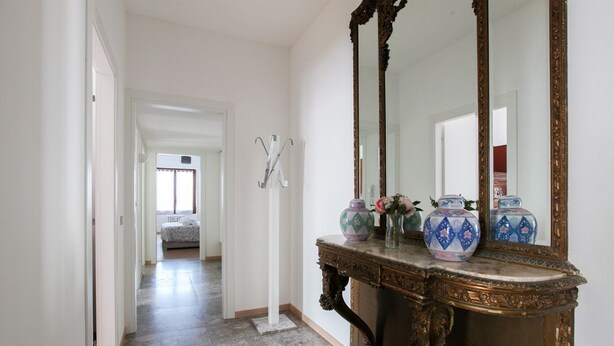 A hallway with a marble floor, a large ornate mirror, and decorative vases on a console table. - New Fashion District 3 BDRS (Milano)