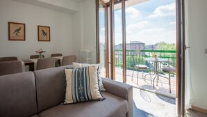 A living room with a sofa, a dining table with chairs, and a balcony with a table and chairs. - New Fashion District 3 BDRS (Milano)