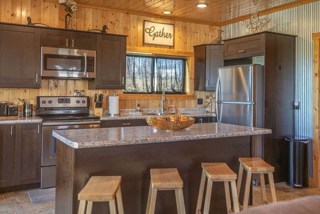Una cucina con pareti in legno, un'isola centrale con sgabelli, elettrodomestici in acciaio inossidabile e una finestra con tende.