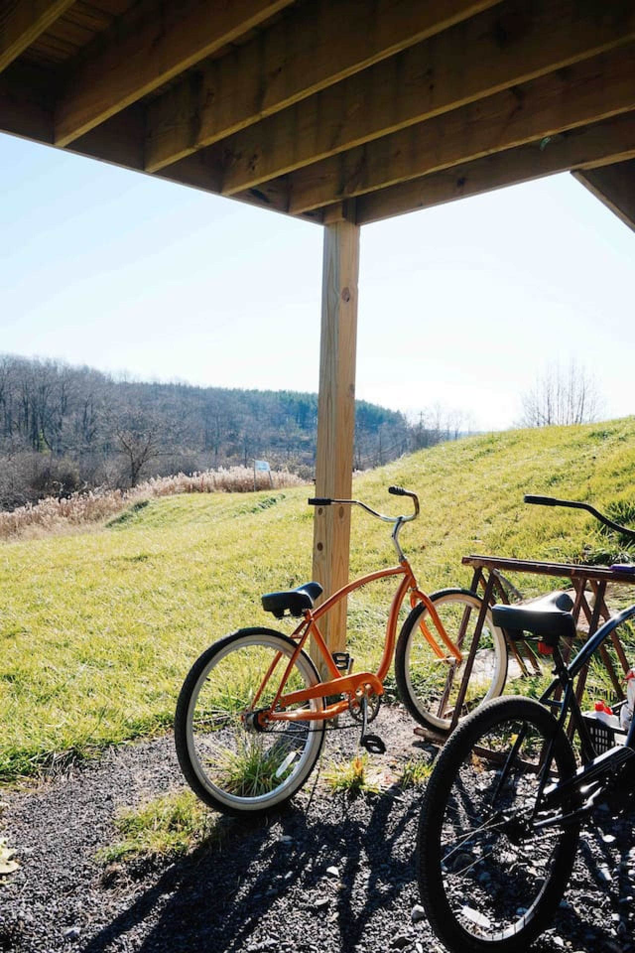 A bicycle parked under a wooden structure with a view of a grassy field and hills in the background.