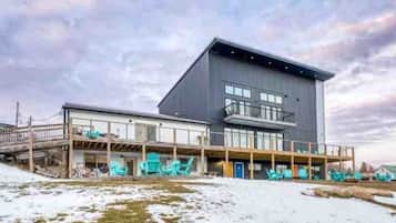 Een modern gebouw met een plat dak, grote ramen en een overdekt terras met stoelen.
