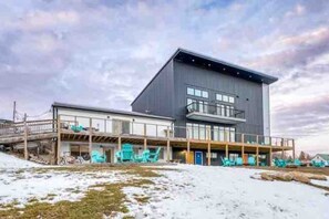 Een modern gebouw met een plat dak, grote ramen en een overdekt terras met stoelen.