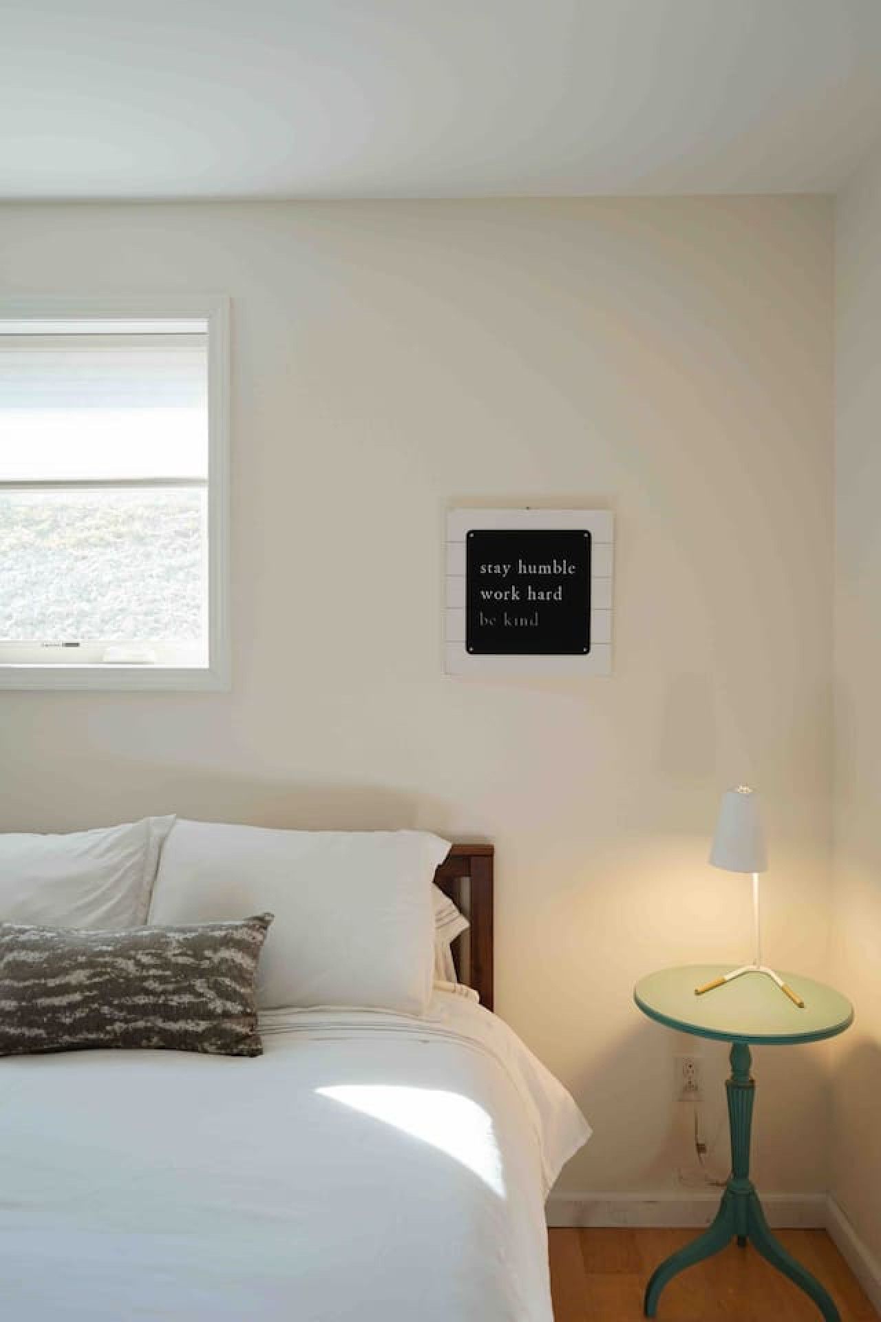 A bedroom with a bed, a bedside lamp, and a motivational quote on the wall.
