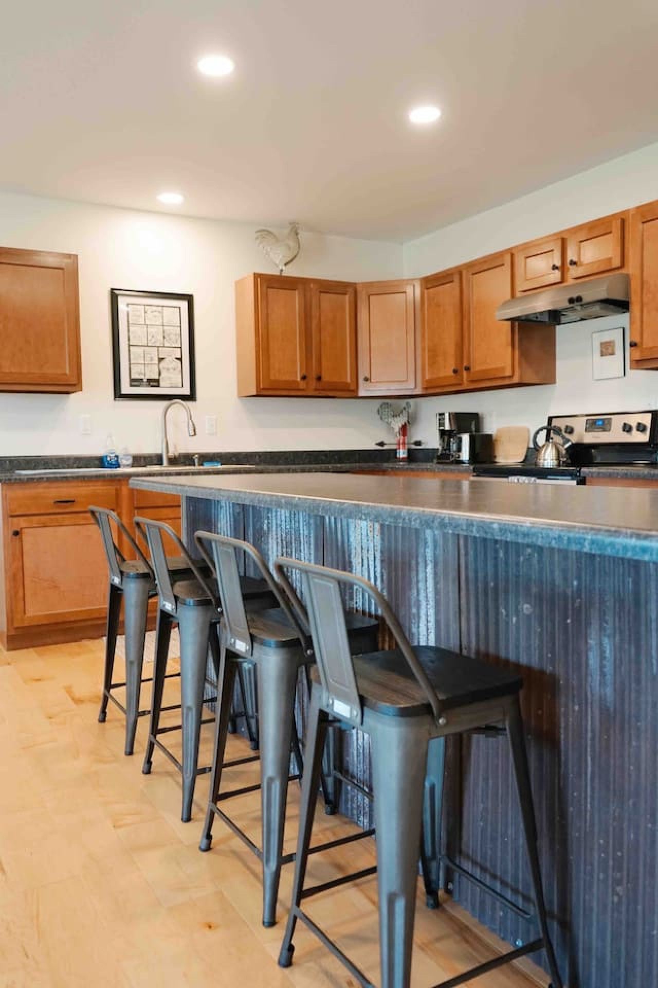 A kitchen with wooden cabinets, a bar area with stools, and a stainless steel range hood.