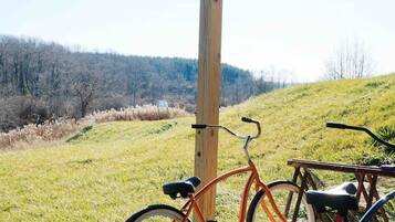 Een fiets geparkeerd onder een houten constructie met uitzicht op een grasveld en heuvels.
