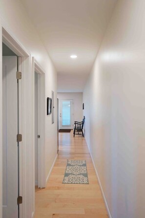 Un couloir doté d’un plancher en bois, d’un tapis à motifs et d’une porte au fond.