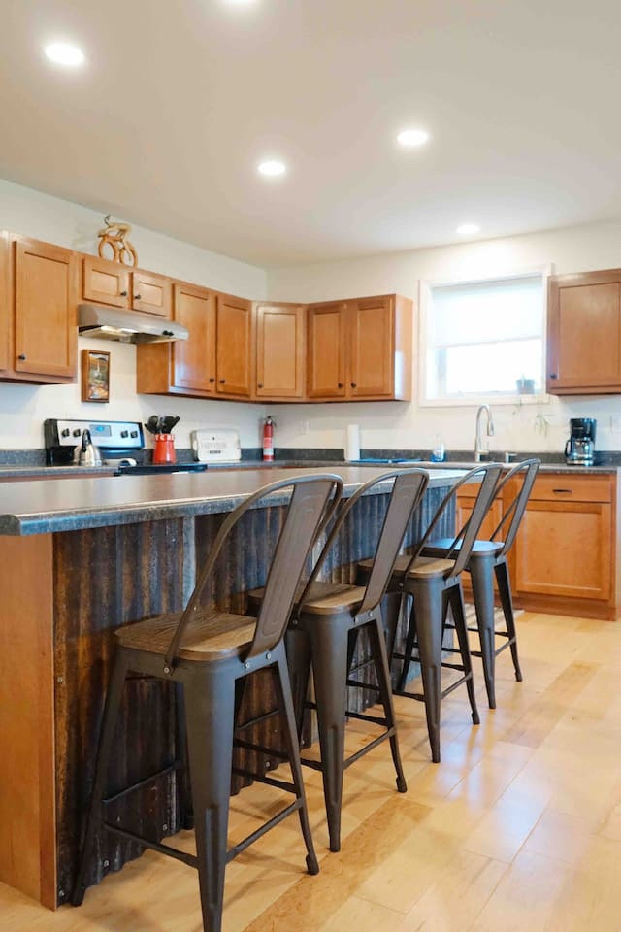 A kitchen with wooden cabinets, a central island with bar stools, a stove, and a window.