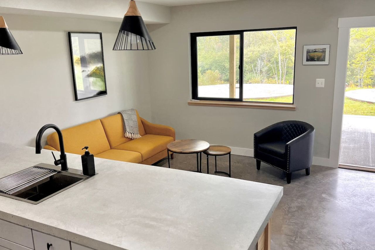 A modern kitchen with a built-in island, a sofa, a small round table, and a black armchair.