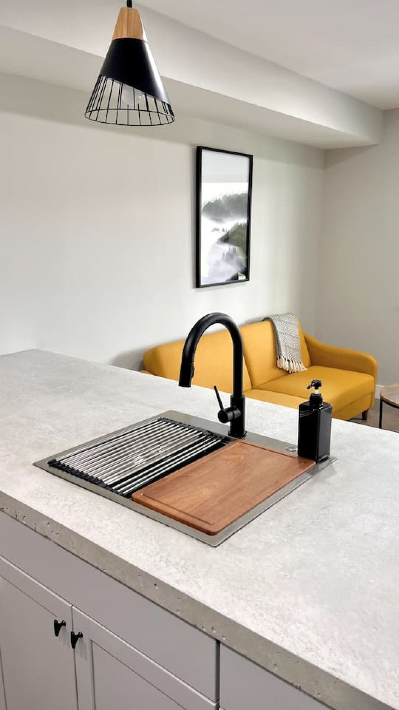 A kitchen with a modern faucet, a wooden cutting board, and a yellow sofa in the background.