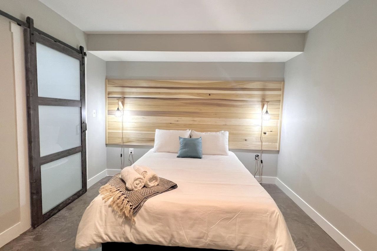 A hotel room with a bed, a wooden headboard, a sliding door, and a bedside lamp.