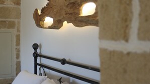A bed with white bedding and a headboard against a wall with exposed brick. - Luxury B&B Casina il Mandorlo (Nardò)