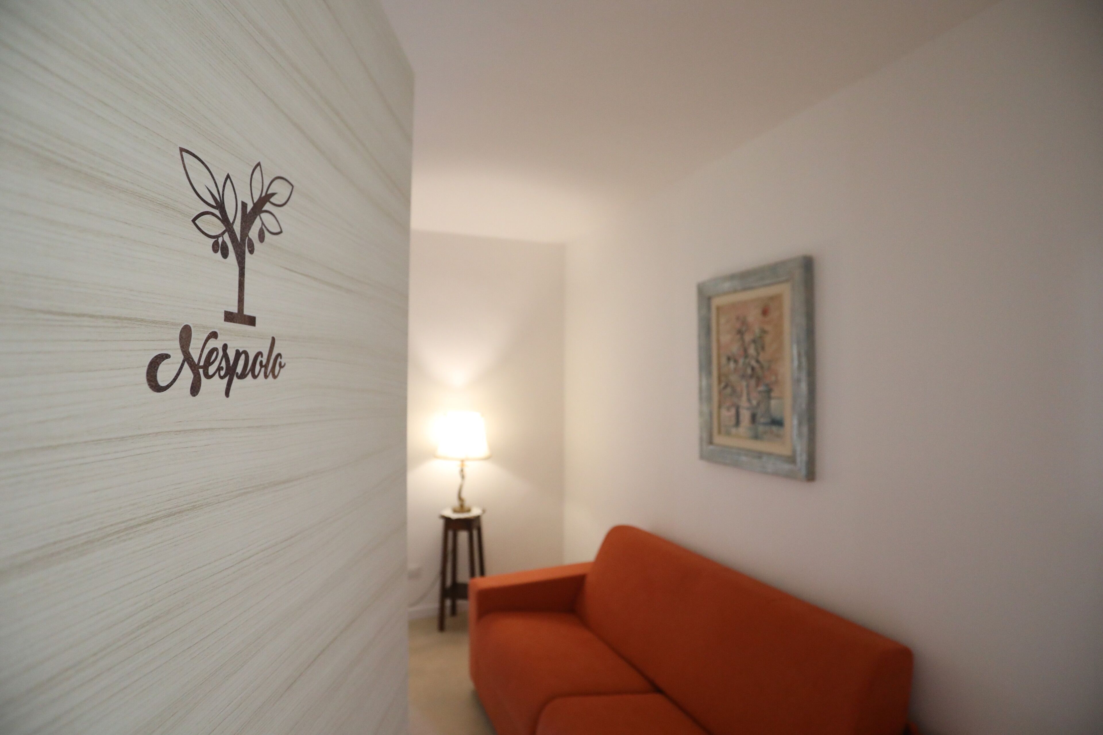 Une pièce avec un mur blanc à la texture particulière, un tableau encadré, un canapé orange et une lampe.