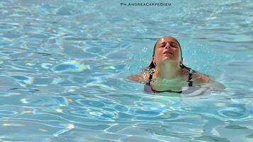 Una persona nuota in una piscina con acqua cristallina e increspature visibili.