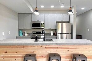 A modern kitchen with grey cabinets, stainless steel appliances, and a central island with stools.