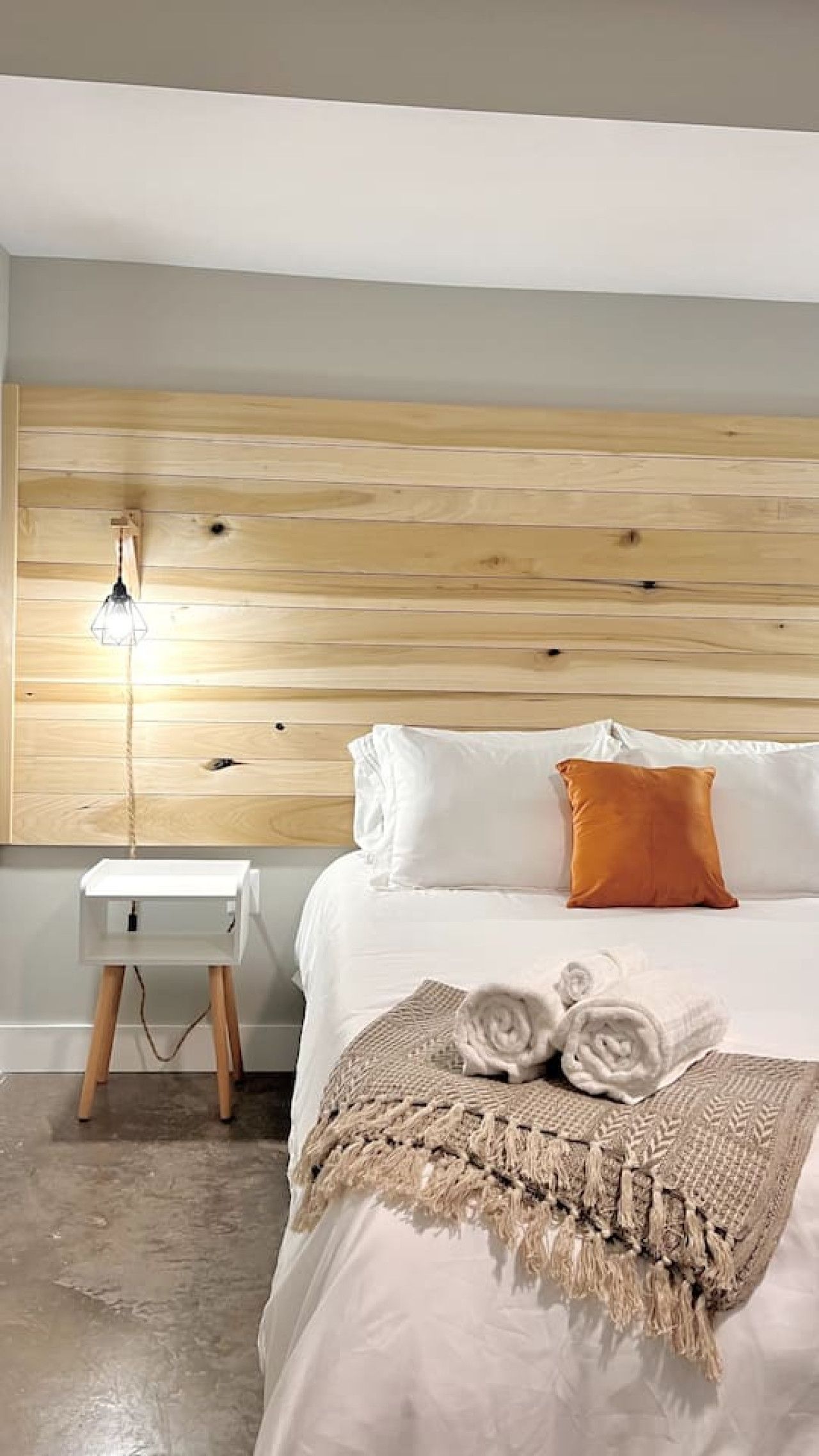 Une chambre à coucher avec une tête de lit en bois, une table de chevet avec une lampe, du linge de lit blanc et une serviette enroulée sur le lit.