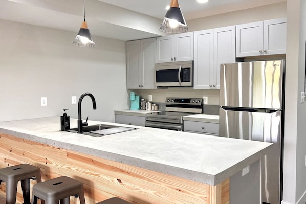 Una cocina moderna con una isla central, electrodomésticos de acero inoxidable y taburetes de madera.