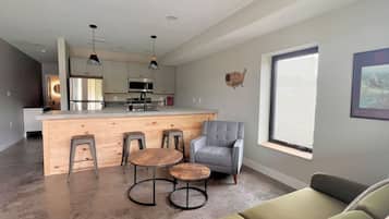 Een moderne keuken met een centraal eiland, barkrukken en een grijze fauteuil.