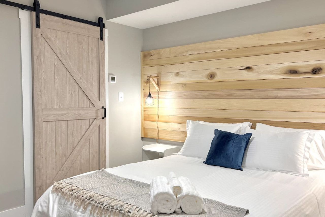 A hotel room with a bed, a wooden headboard, a nightstand, and a sliding barn-style door.